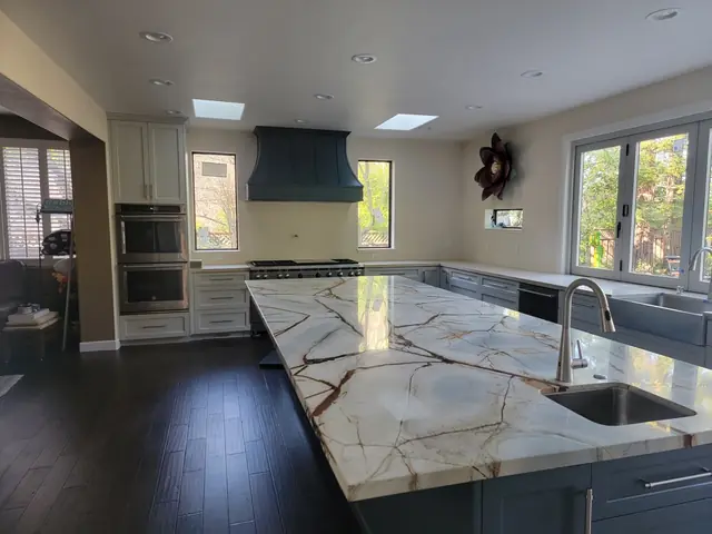Remodeled kitchen with a long blue island, veined countertops and a blue range hood